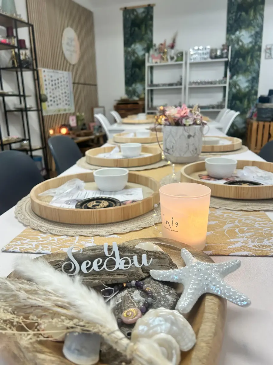 Liebevoll gedeckter Workshop-Tisch bei SeeYou Perlen mit Holztabletts, Kerze, Muscheln und einem SeeYou-Schriftzug.